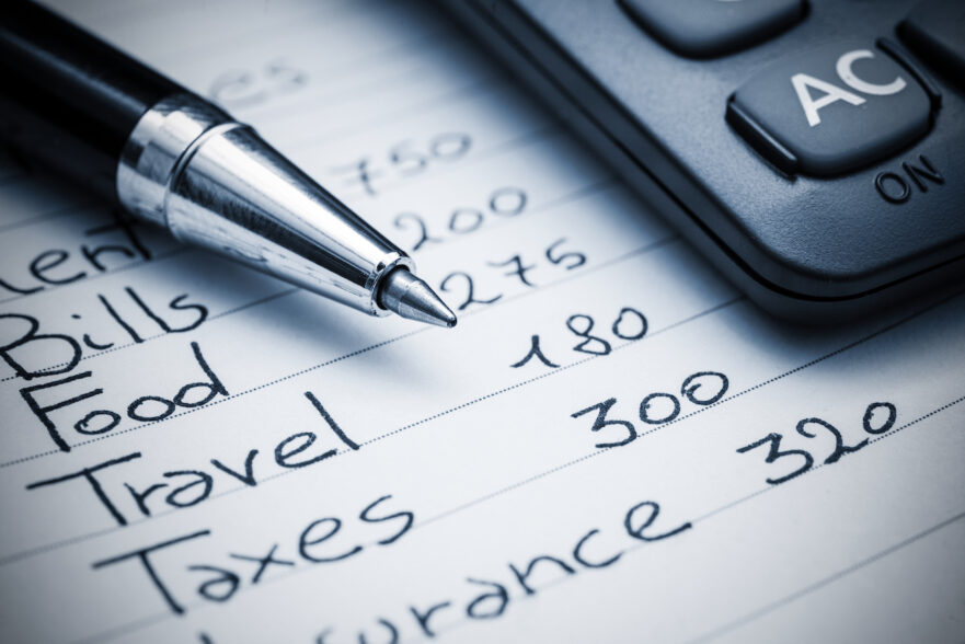 A list of items in a household budget written in black ink. A pen and calculator sit on top of the list.
