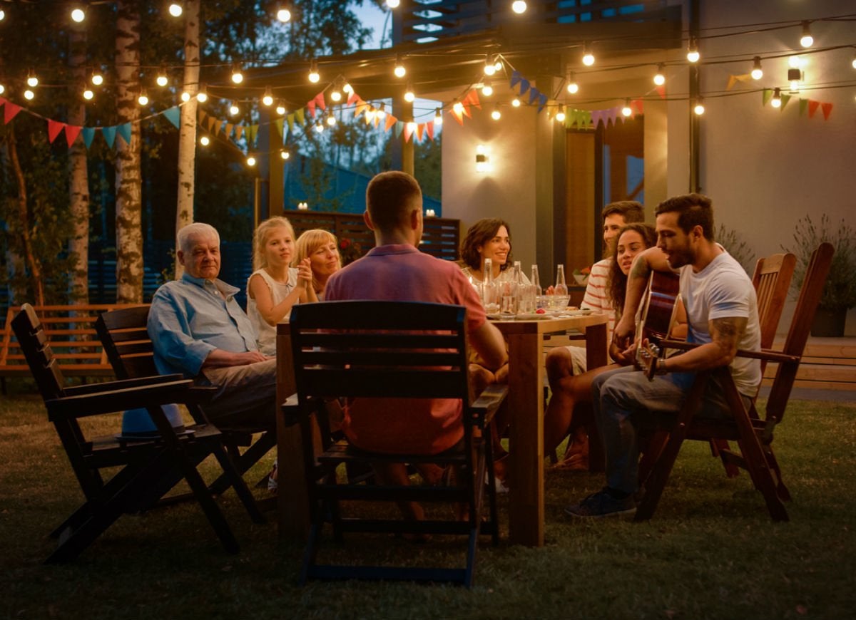 Family eating at a backyard dining table lit with string lights.