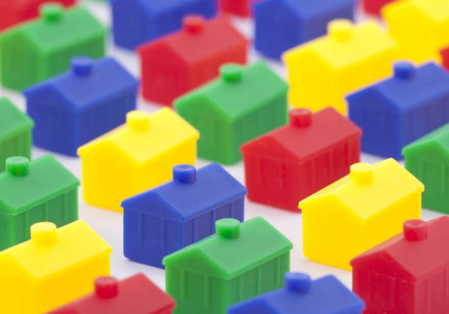 Tiny plastic houses in blue, red, green, and yellow sit in neat lines on a white surface.
