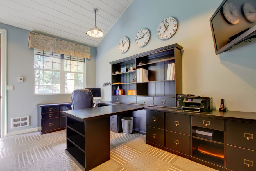 A home office with dark wood furniture, carpet, and a large window behind the desk.