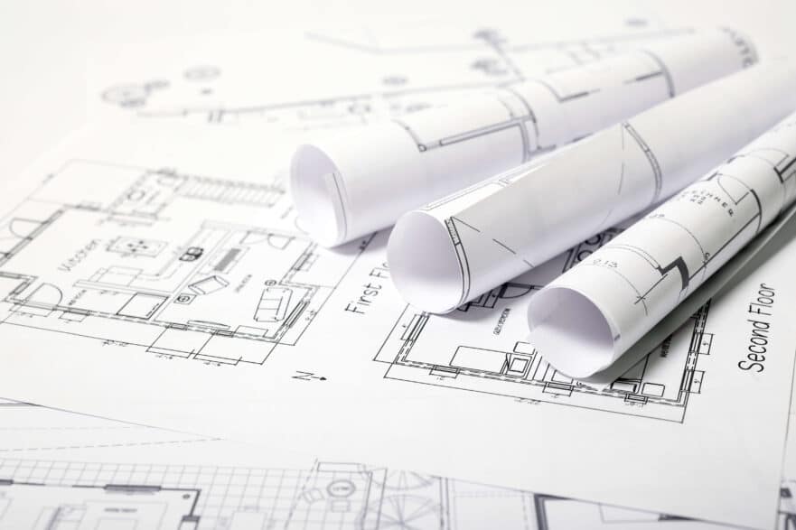 Three rolled-up architectural plans on top of a design for a two-story new home.