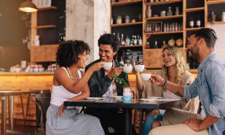 Young people sitting at cafe table and having coffee together. Group of friends making a toast with coffee.